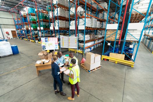 High angle view of mature diverse staffs discussing over document in warehouse. This is a freight transportation and distribution warehouse. Industrial and industrial workers concept