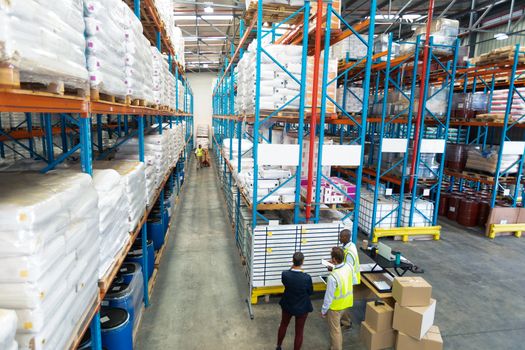 High angle view of diverse warehouse staff discussing over whiteboard in warehouse. This is a freight transportation and distribution warehouse. Industrial and industrial workers concept