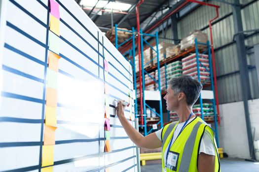 Side view of pretty mature Caucasian female staff writing on whiteboard in warehouse. This is a freight transportation and distribution warehouse. Industrial and industrial workers concept