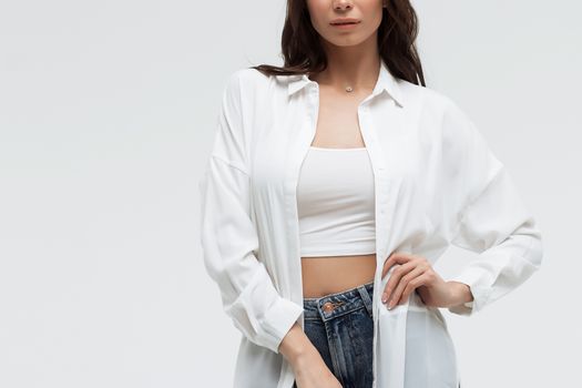 Crop confident long haired woman in white shirt and lingerie and jeans with crossed hands on white background
