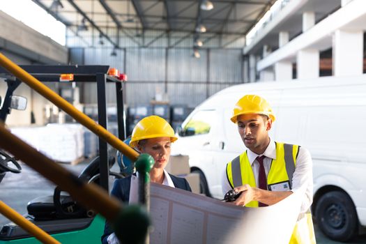 Front view of Caucasian female manager and Caucasian male supervisor discussing over inventory chart in warehouse. This is a freight transportation and distribution warehouse. Industrial and industrial workers concept