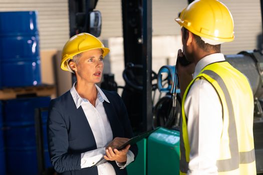 Front view of Caucasian female manager and Caucasian male supervisor interacting with each other in warehouse. This is a freight transportation and distribution warehouse. Industrial and industrial workers concept