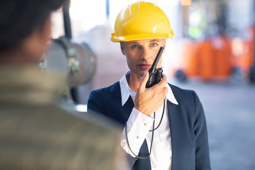Front view of Caucasian Mature female manager talking on walkie talkie in warehouse. This is a freight transportation and distribution warehouse. Industrial and industrial workers concept