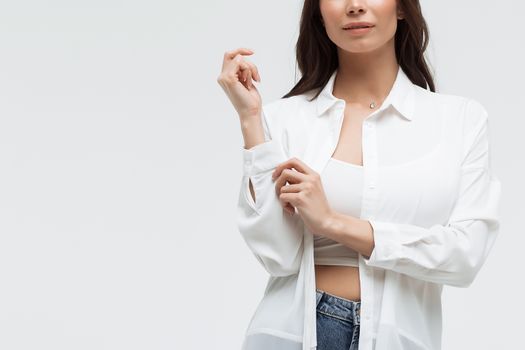 Crop confident long haired woman in white shirt and lingerie and jeans with crossed hands on white background