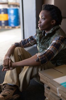 Close-up of thoughtful African-american female worker sitting in warehouse. This is a freight transportation and distribution warehouse. Industrial and industrial workers concept