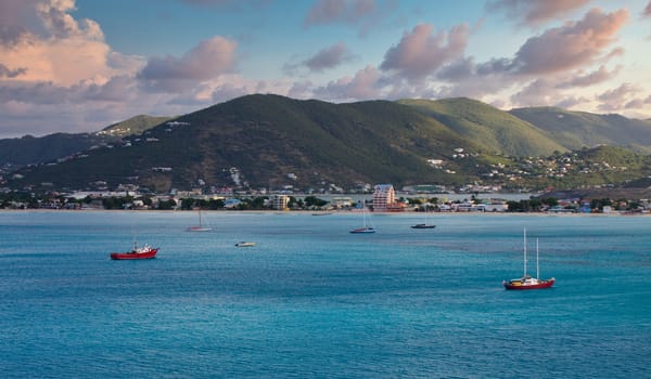 Red sailboats in blue water off tropical coast in morning light