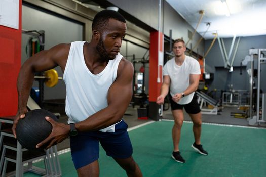 Front view of handsome diverse male athletics exercising together with exercise ball in fitness center. Bright modern gym with fit healthy people working out and training