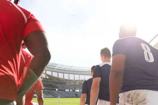 Low angle view of diverse male rugby players standing in a row at stadium while mentally preparing for match on a sunny day.