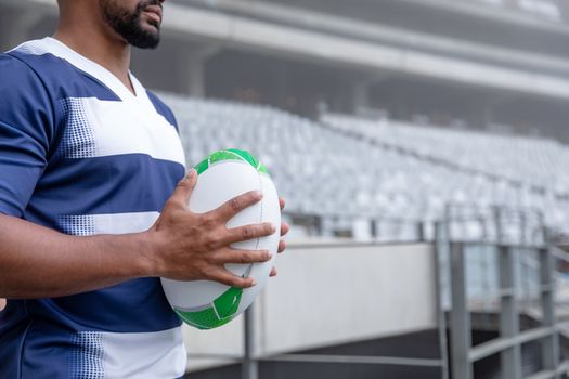 Mid section of African American male rugby ball player holding a rugby ball in stadium