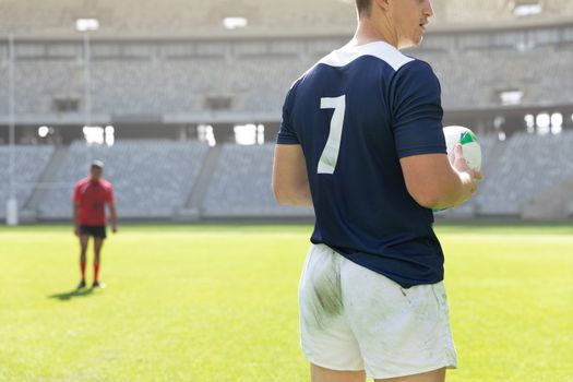 Mid section close up of handsome Caucasian male rugby player holding a rugby ball in the stadium on a sunny day.