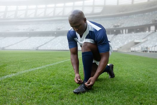 Front view of African american male rugby player tying shoelaces in the stadium