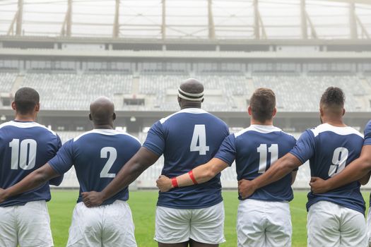 Rear view of group of diverse male rugby players taking pledge together in stadium
