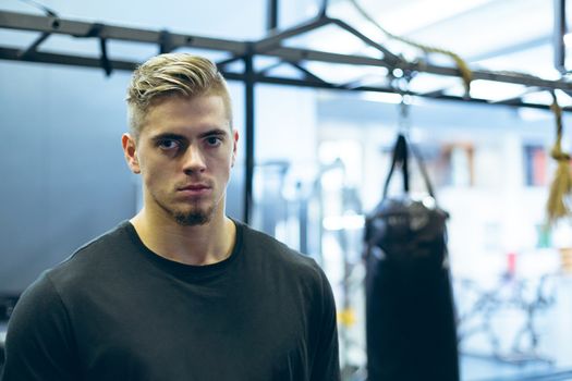Portrait of handsome young Caucasian male athletic looking at camera in fitness center. Bright modern gym with fit healthy people working out and training