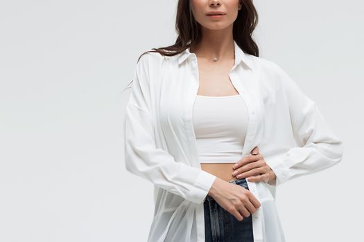 Crop confident long haired woman in white shirt and lingerie and jeans with crossed hands on white background