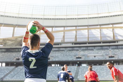 Rear view of Caucasian male rugby player throwing rugby ball while diverse rugby players are waiting for him to throw it in stadium