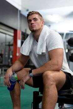 Close-up of thoughtful young Caucasian male athletic relaxing in fitness center. Bright modern gym with fit healthy people working out and training