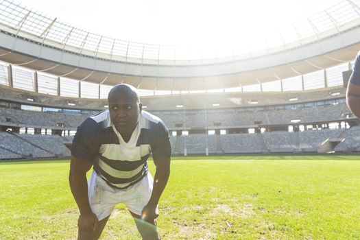 Front view of tired African American male rugby player standing with his hands on thighs in stadium on sunny day.
