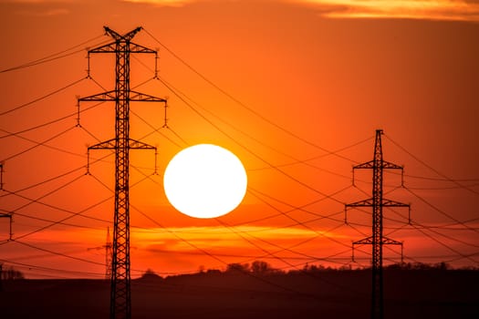 View at a Silhouette of Electric Lines and Column Pillar during Sunset with Clouds on the Sky.Beautiful sunset Nature . Beautiful rural landscape with electric pillars .