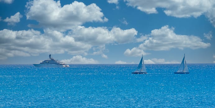 Two white sailboats and a luxury yacht sailing across a deep blue bay