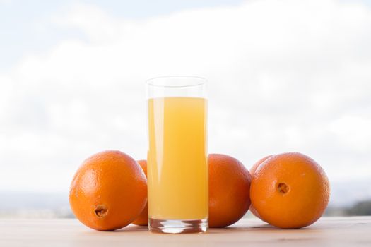 glass of delicious orange juice and oranges on table in garden