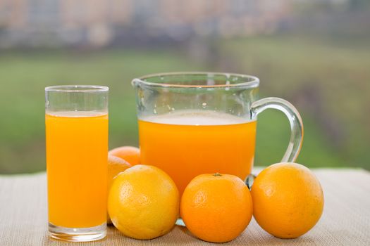 glass of delicious orange juice and oranges on table in garden