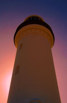 A vertical low angle shot of a lighthouse against a sunset sky background