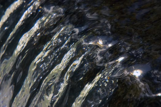 Ultra closeup shot of crystal clear water flowing across a ledge and reflecting the sun