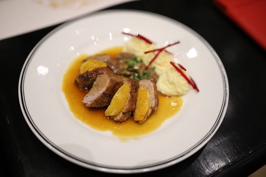 Roasted duck topped with orange sauce and mashed potatoes Decorate the dish looks appetizing on the white plate in the restaurant. Selective focus.