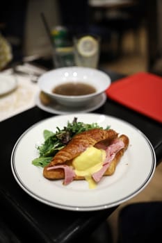 Croissants with eggs benedict and ham filling look appetizing on a white dish in a restaurant. Selective focus.