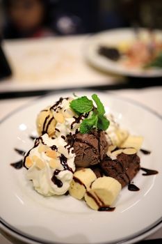 Chocolate ice cream and sliced bananas Garnish with mint leaves. With white mousse and sliced almonds in a white plate Topped with chocolate sauce to look delicious. Selective focus.