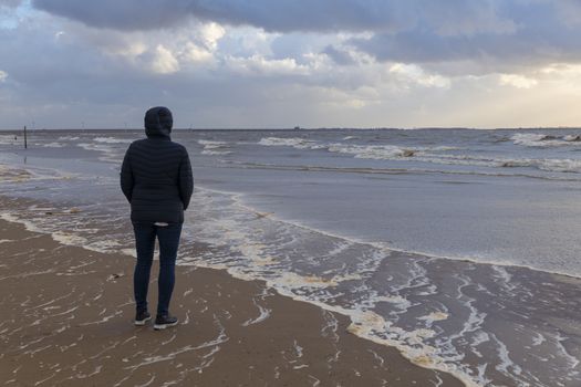 woman at the beach during a storm with high sea water level in rockanje in holland, the northsea is here very hig in stead of a wide beach