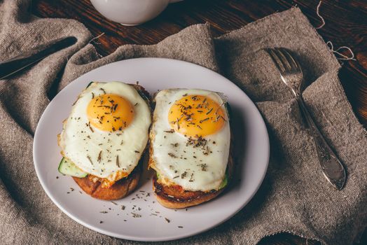 Italian toasts with vegetables and fried eggs on white plate and cup of coffee over grey rough cloth.