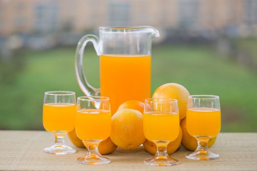 glass of delicious orange juice and oranges on table in garden