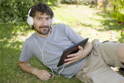 young man holding a tablet with headphones, outdoor