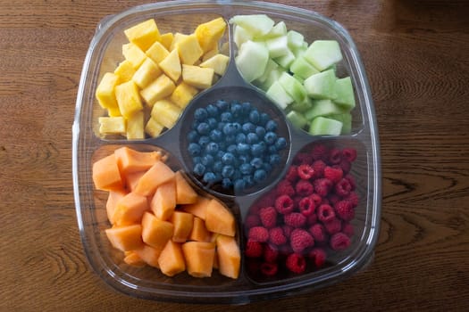Sliced fruits and blueberries in the center in a large plate divided into sections