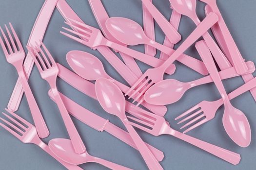 Background from reusable recyclable pink forks, spoons, knifes made from corn starch on grey paper. Eco, zero waste, alternative to plastic concept. Flat lay, top view. Horizontal. Closeup.