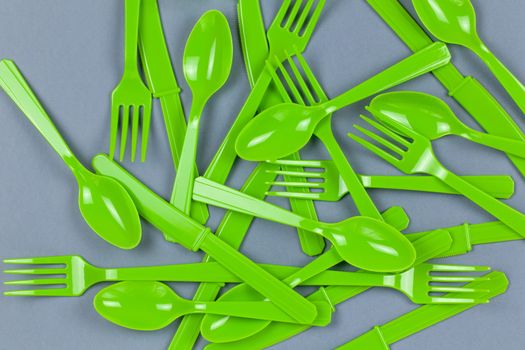 Background from reusable recyclable green forks, spoons, knifes made from corn starch on grey paper. Eco, zero waste, alternative to plastic concept. Flat lay, top view. Horizontal. Closeup.