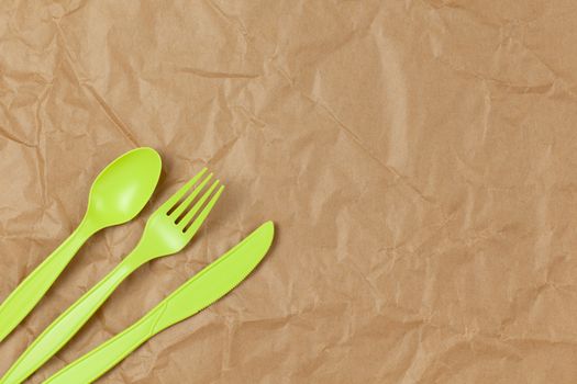 Reusable recyclable green fork, spoon, knife made from corn starch on brown crumpled craft paper, copy space. Eco, zero waste, alternative to plastic concept. Flat lay. Horizontal. Closeup.