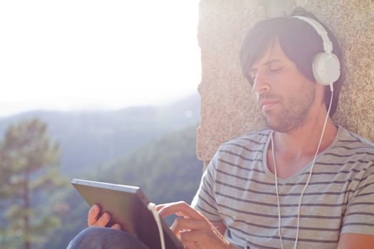 young man working with a tablet pc listening music with headphones, outdoor