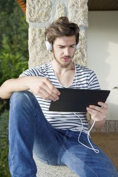 young man relaxing with a tablet pc listening music with headphones, outdoor