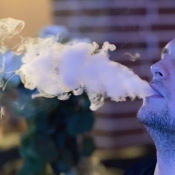 Close-up of a man smoking a traditional hookah pipe, man exudes smoke, hookah lifestyle and smoking concept. Selective focus