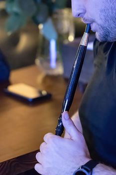 Close-up of a man smoking a traditional hookah pipe, man exudes smoke, hookah lifestyle and smoking concept. Selective focus