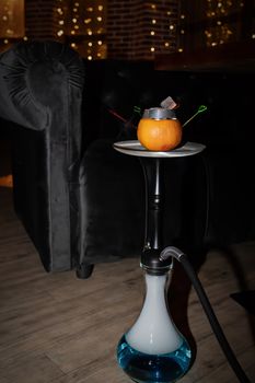 Oriental hookah with orange stands on the floor against the background of lighting in a cafe. Dark night is a magical scene.