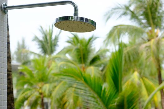 Close-up of Detail of a water shower head on seashore. Outdoor shower palm trees blurry background.