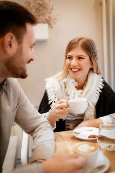 Young smiling woman drinking coffee and talking with her boyfriend at cafe.