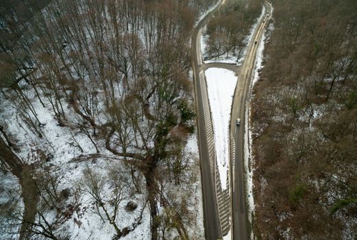 Drone aerial top view of a road going through forest with snow.