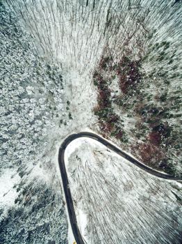 Drone aerial top view of a road going through forest surrounded by a snow in wild park.