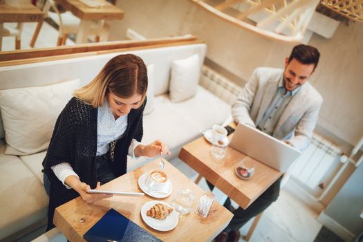 Young businesspeople surfing the internet on a break in a cafe. Smiling woman using digital tablet and drinking coffee. Man working at laptop. Selective focus. Focus on businesswoman.