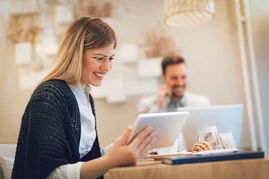 Beautiful young smiling woman using digital tablet and drinking coffee in a cafe. Selective focus. Focus on businesswoman.