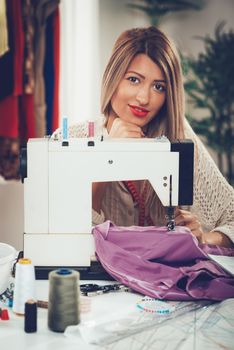 Portrait of a young beautiful smiling girl sew with a sewing machine. Looking at camera.